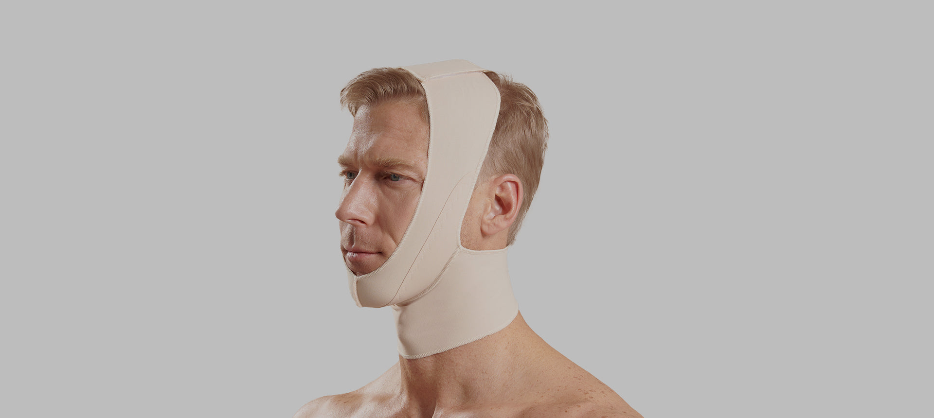 A man wearing a post-surgical compression face mask that covers his jawline and neck and wraps around with a hook-&-loop closure on the top of his head.