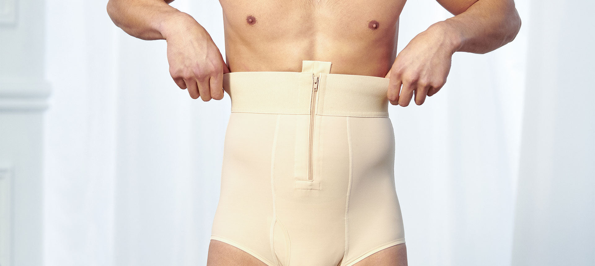 A close-up picture of a man wearing a post-surgical compression girdle. He is adjusting the soft, elastic waistband with his hands.